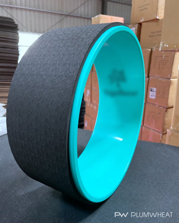 Side view of a turquoise yoga wheel with the buyer's branding blurred for privacy.