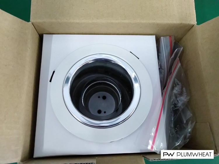 Downlight housing inside an open cardboard box with a white packaging insert and bagged accessories
