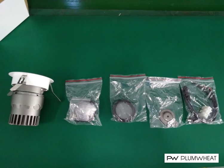 Downlight housing and individually bagged accessories arranged on a green inspection table