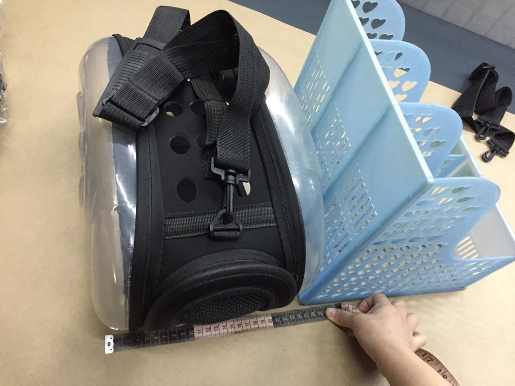 Inspector using a measuring tape to check the dimensions of a pet carrier.